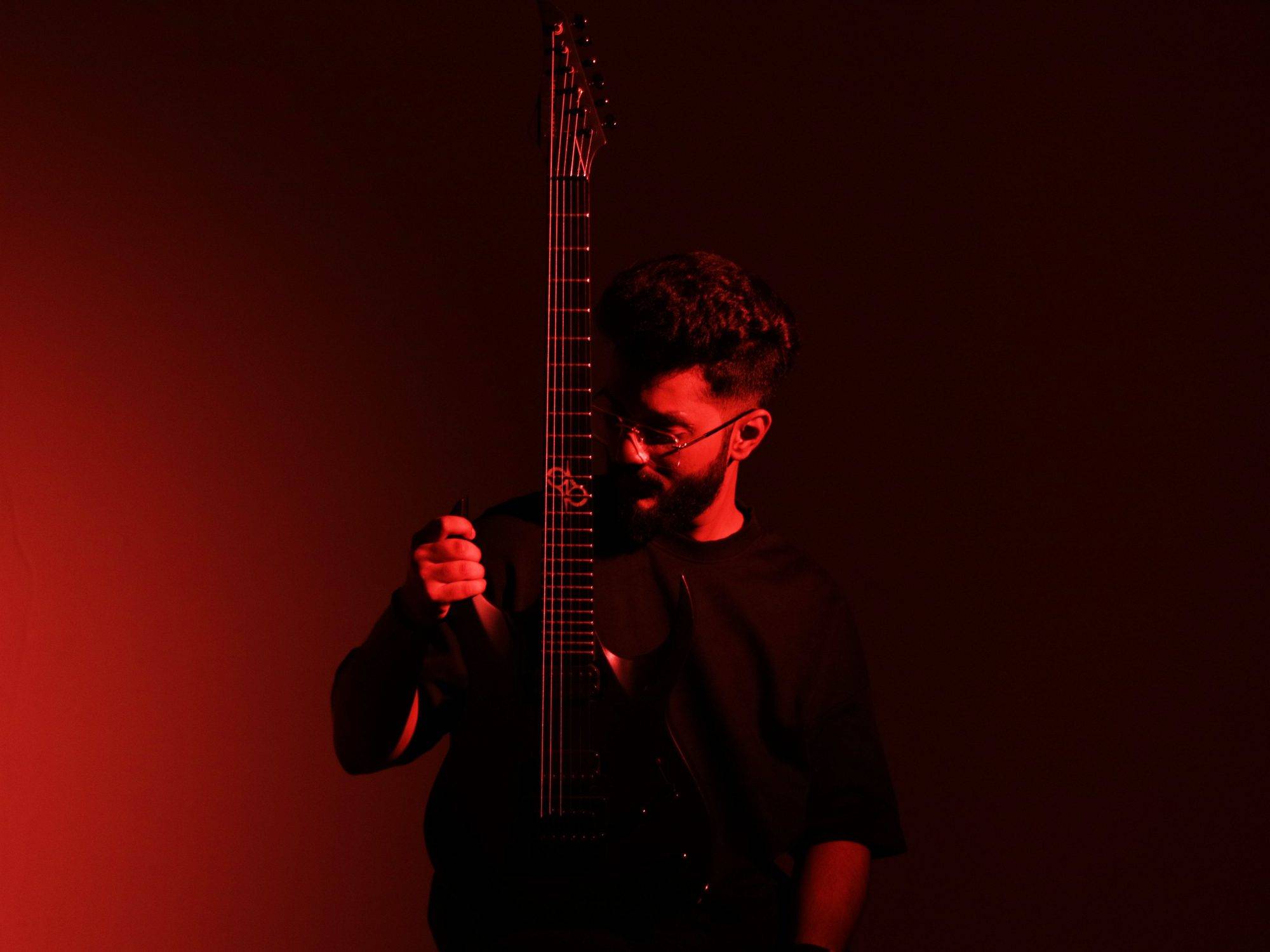 Ezekiel Bernard holding his guitar upright in red light