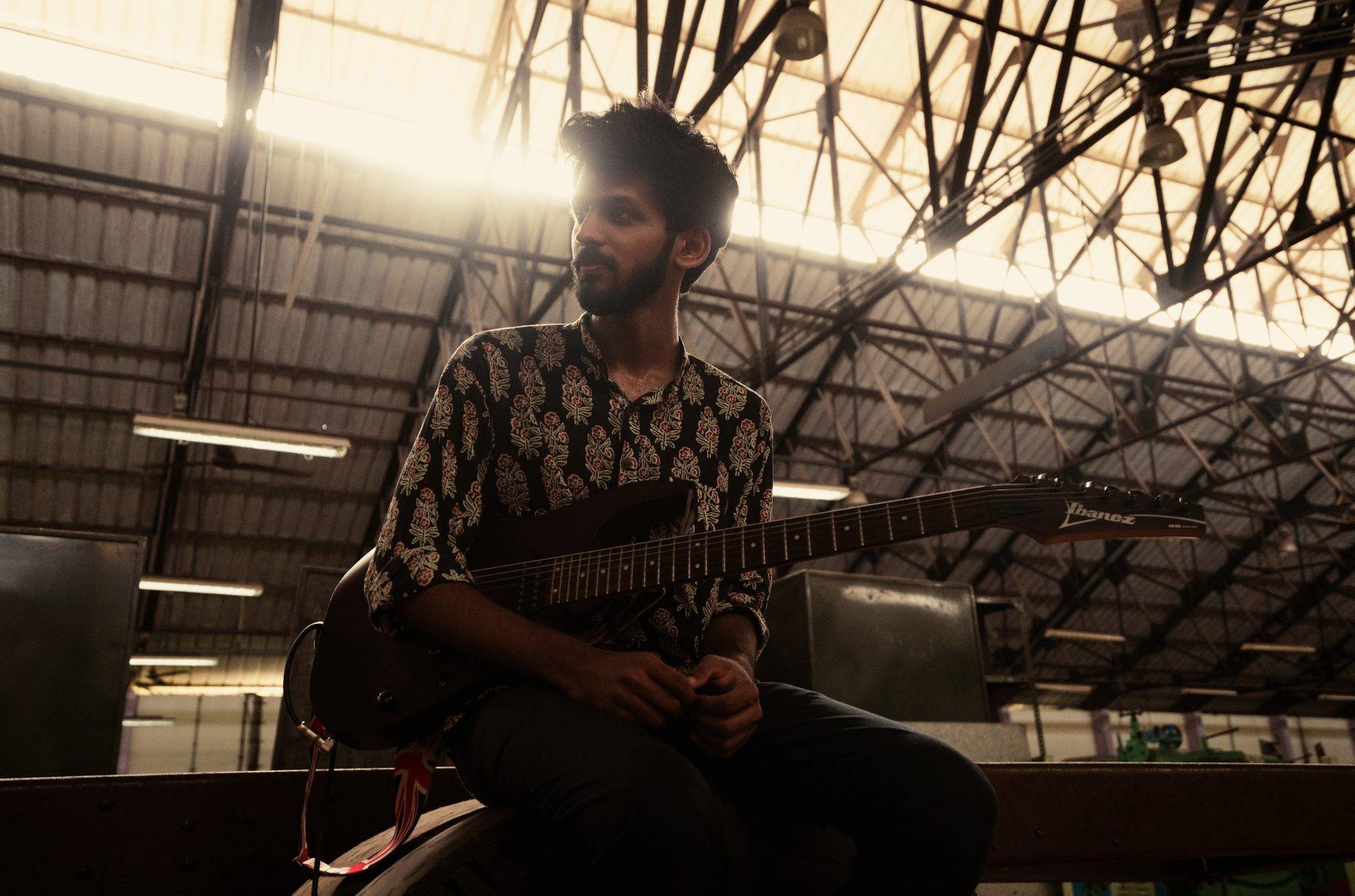 Sreeram Vijay seated with his Ibanez guitar in a warehouse